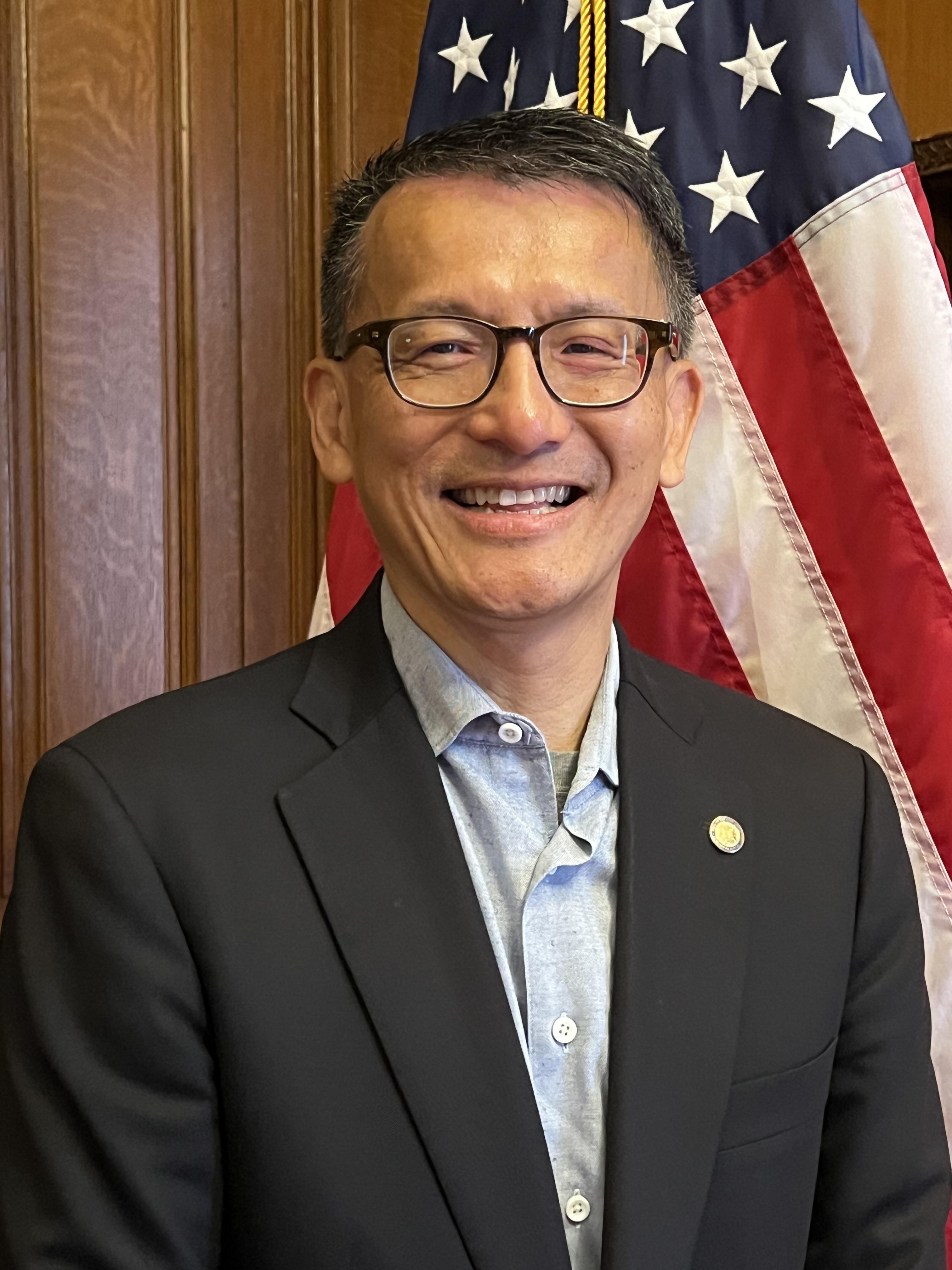 Commissioner Leung is a middle aged man standing in front of the US flag